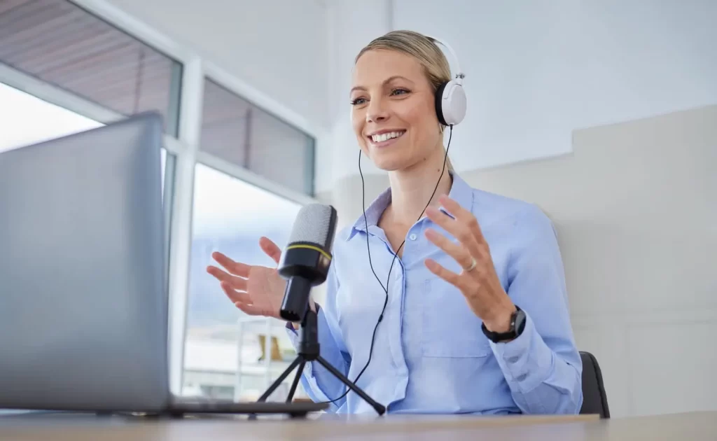 Eine Frau mit Kopfhörern spricht in einem hellen Büro vor einem Computer in ein Mikrofon.