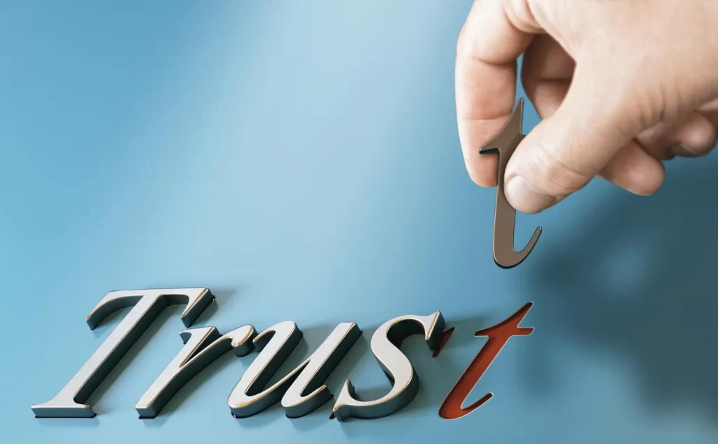 Eine Hand fügt das letzte T zum englischen Wort Trust hinzu. Trust bedeutet Vertrauen.