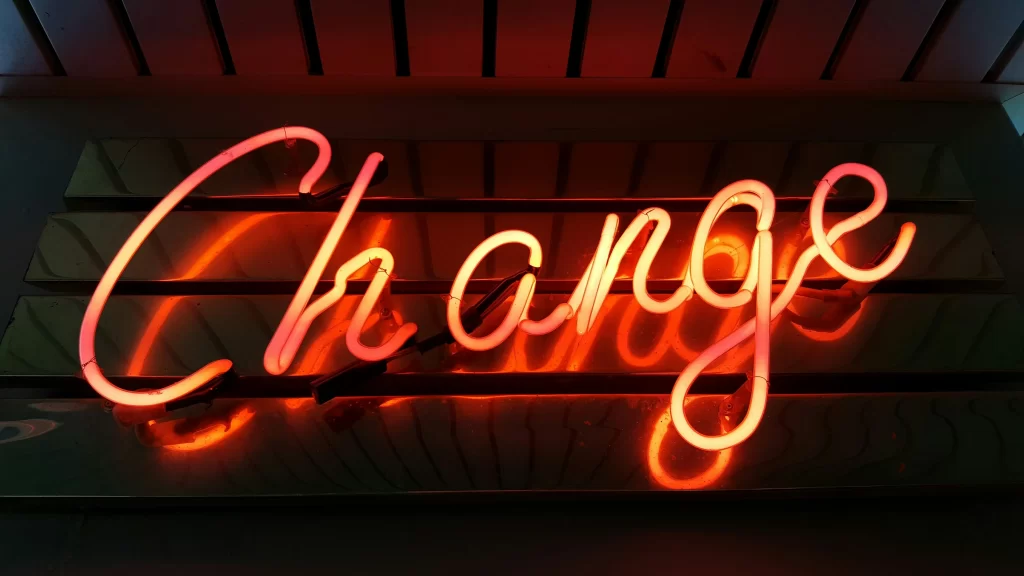 Neonschild mit dem Wort „Change“ vor einem Lamellenhintergrund.