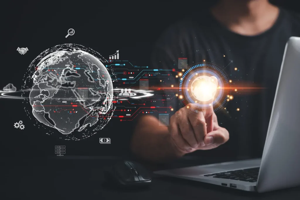 Eine Person interagiert mit einer digitalen Schnittstelle. Ihr Finger berührt einen leuchtenden Punkt auf der Schnittstelle, auf der futuristische Grafiken und ein digitaler Globus angezeigt werden. Vor ihr stehen ein Laptop und eine Maus.