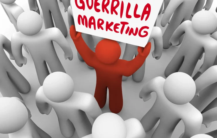 Eine rote Figur in einer Menschenmenge hält ein Schild mit der Aufschrift „Guerilla Marketing“ hoch. Die umliegenden Figuren sind grau.