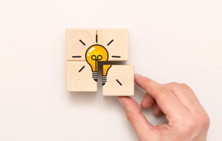 Eine Hand ordnet Holzklötze mit der Abbildung einer Glühbirne an, die eine Idee oder Innovation symbolisiert.