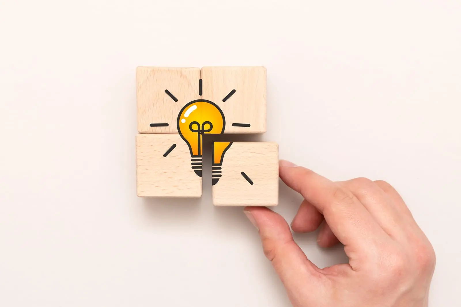Eine Hand ordnet Holzklötze mit der Abbildung einer Glühbirne an, die eine Idee oder Innovation symbolisiert.