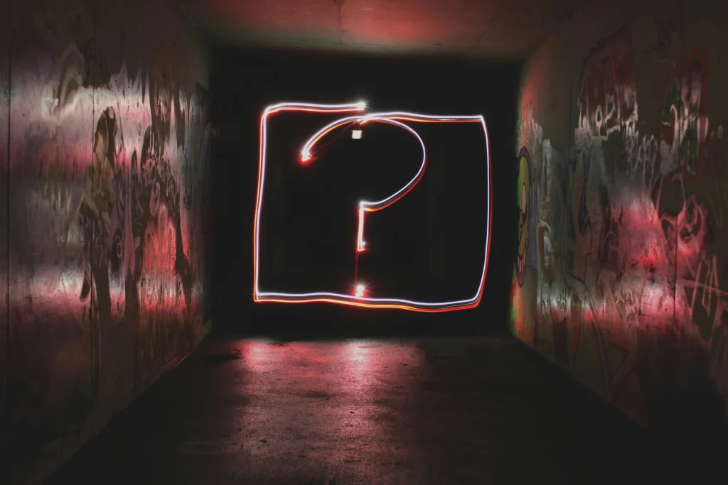 Neon-Fragezeichen-Lichtmalerei in einem dunklen, mit Graffiti bedeckten Tunnel.
