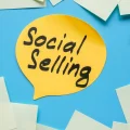 Gelbe Sprechblase mit dem Text „Social Selling“ auf blauem Hintergrund, umgeben von leeren Haftnotizen.