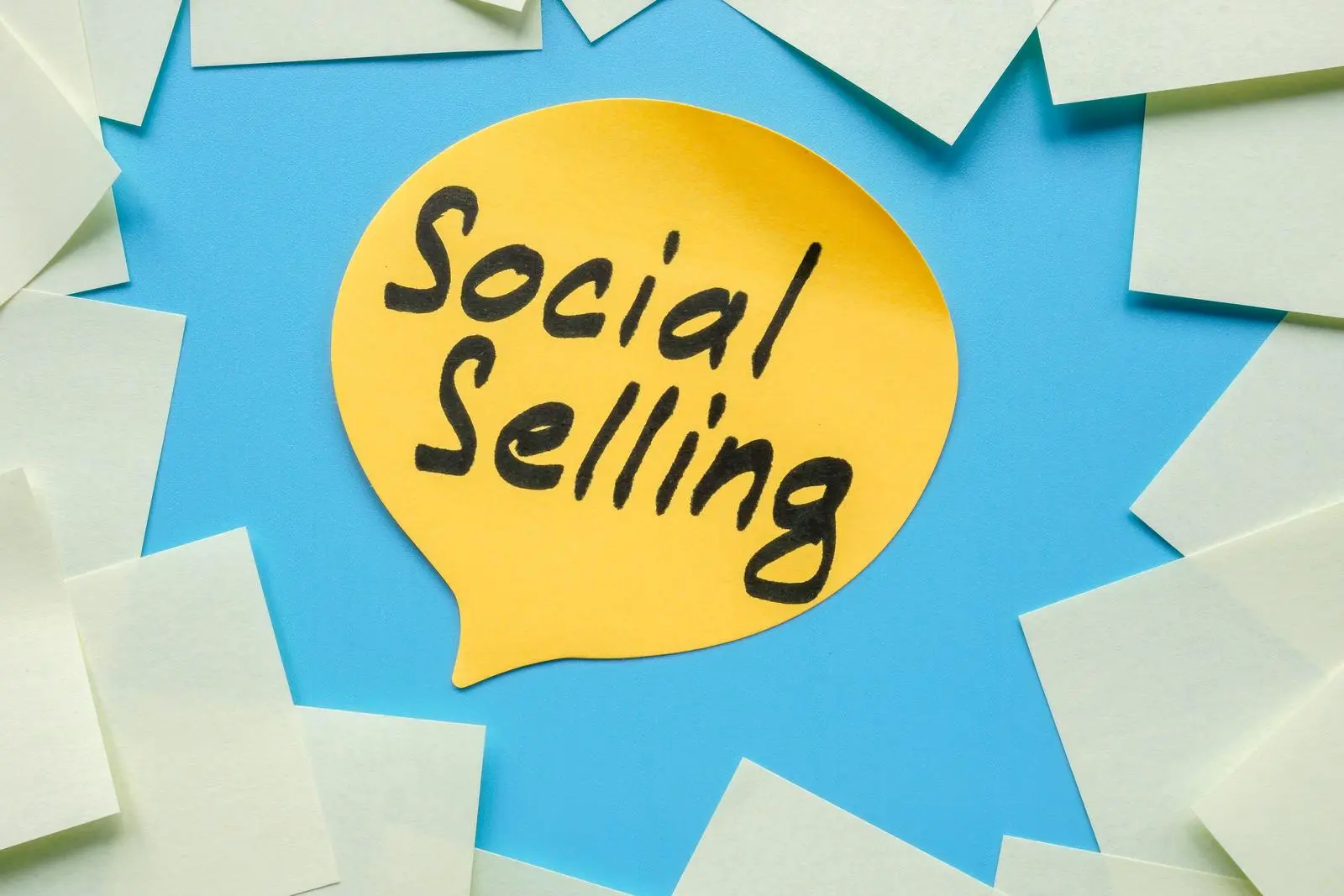 Gelbe Sprechblase mit dem Text „Social Selling“ auf blauem Hintergrund, umgeben von leeren Haftnotizen.