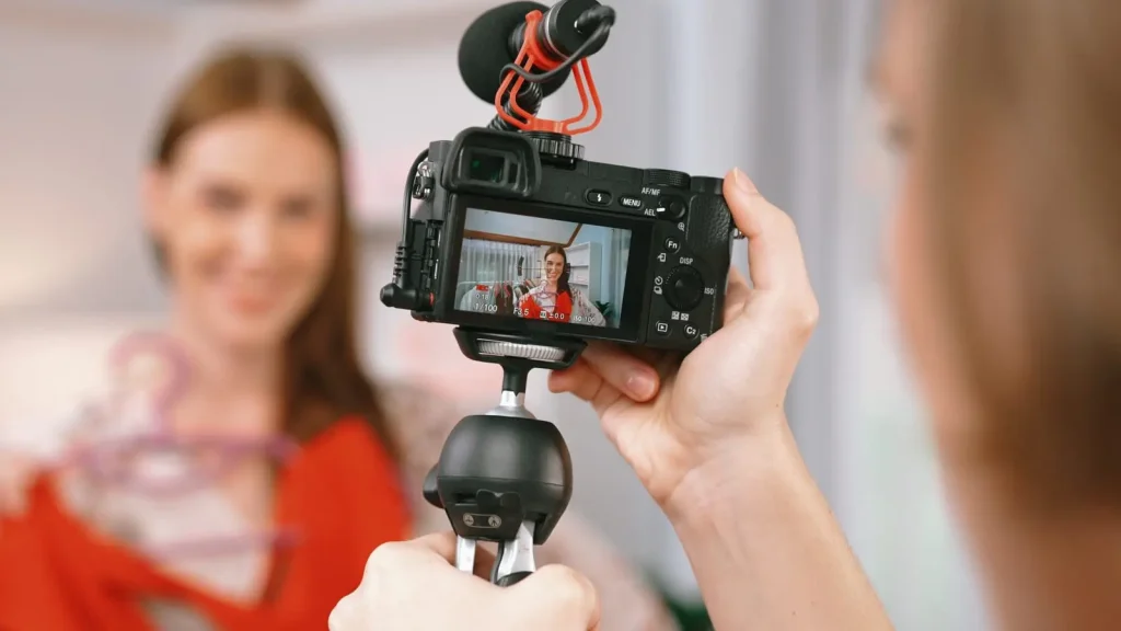 Person, die mit einer auf einem Handstabilisator montierten Kamera ein Video einer Frau aufnimmt, die einen Kleiderbügel mit roter Kleidung hält.