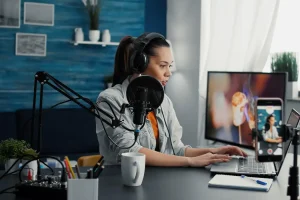 Eine Frau nimmt in einem Heimstudio mit einem Mikrofon, Kopfhörern und einem Laptop einen Podcast oder eine Live-Übertragung auf.