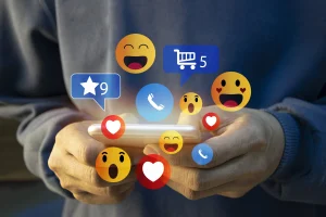 Person, die ein Smartphone verwendet, über dessen Bildschirm verschiedene Social-Media- und Benachrichtigungssymbole schweben, darunter Reaktionen, Einkaufswagen und Telefonsymbole.
