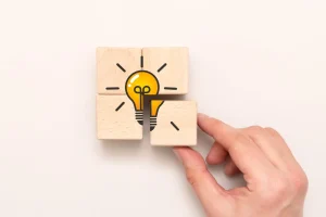 Eine Hand ordnet Holzklötze mit der Abbildung einer Glühbirne an, die eine Idee oder Innovation symbolisiert.